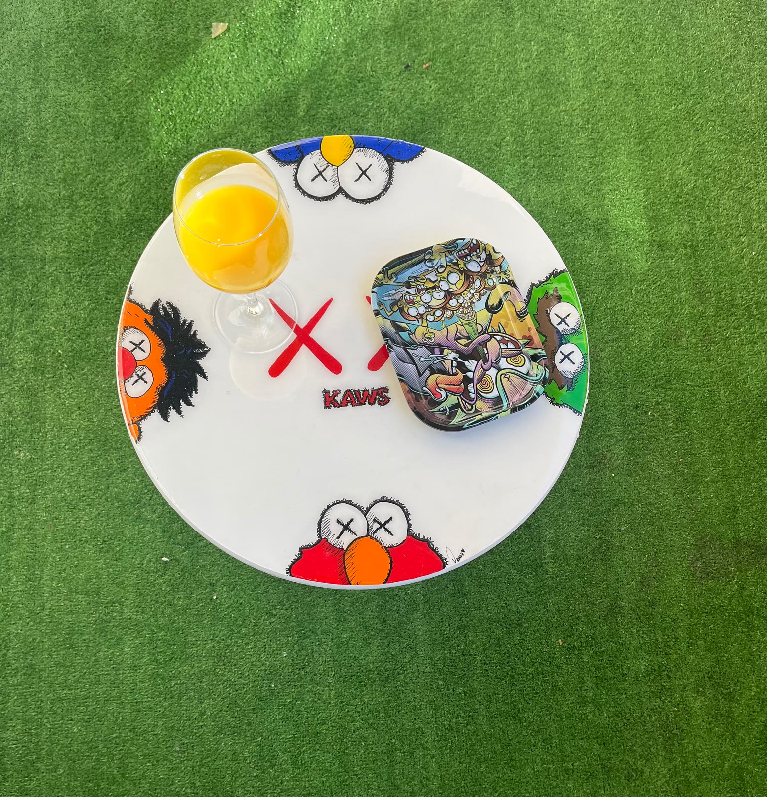 Custom Glitter Table — a white round table with painted figures, on grass.